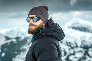 Portrait of a stylish man with a beard and curled mustache in the mountains with snow-covered peaks...
