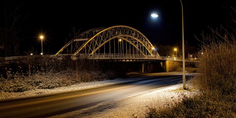 Obraz premium A snow-covered bridge illuminated at night, with a quiet road beside it.