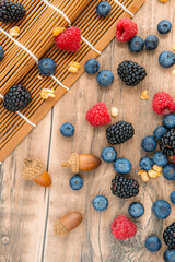Close-up on mix berries: blackberries, blueberries, raspberries and acorns isolated on a wooden table background, vertical image
