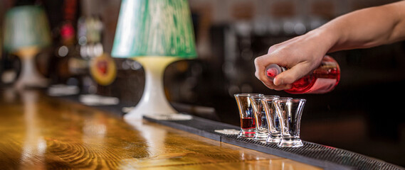 Bartender man pours whiskey to the client of the bar. The concept of service. Bartender pouring strong alcoholic drink into small glasses on bar, shots. Shot glasses with liquor in the bar