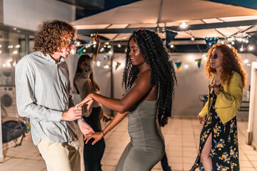 Multi-ethnic friends dancing holding hands latin music at night party