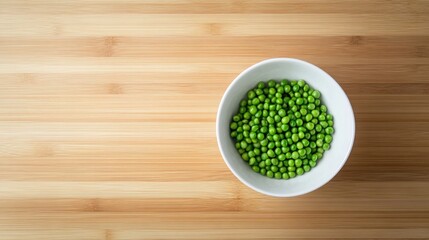 Fresh green peas elegantly arranged in a white bowl on a rustic wooden surface, captured from an overhead perspective.
