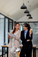 Two asian business women discuss financial management planning.standing and talking about analyzing documents in the workplace office
