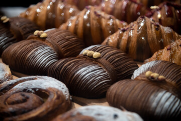 Close-up side view of fresh baked brown butterfly shaped croissants with hazelnuts lying on shelf of bakery or cafe by other puff pastry items. Soft focus. Copy space. Food and pastry background theme