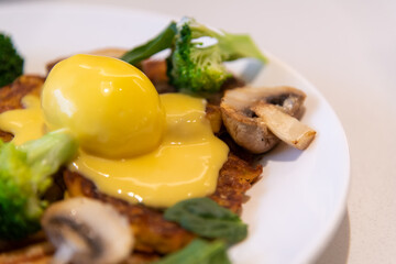 Close-up view of healthy breakfast: boiled egg, fried yam with marrow pancake, fried thin croissant, broccoli, mushrooms, yellow hollandaise sauce and white sour cream (smetana). Food background.