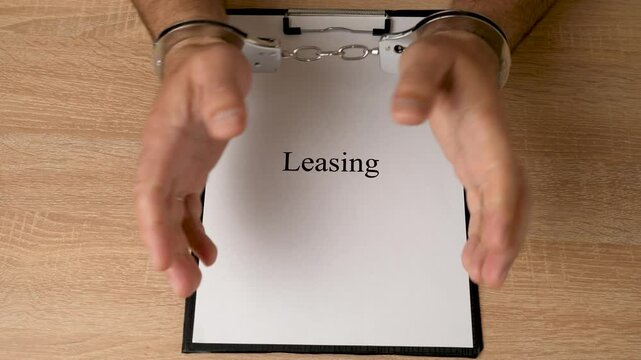 A man in handcuffs holds a document with the inscription "leasing". Concept of dependence on leasing.