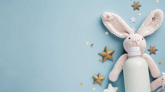 Baby Accessories Concept: Top view photo of a knitted bunny toy, milk bottle, and gold stars on an isolated pastel blue background with copyspace.