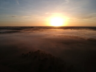 Drone video of a sunrise in the countryside with low fog and an intense yellow sun