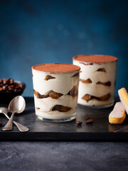Tiramisu dessert in glass on marble cutting board. Blue background. Copy space.