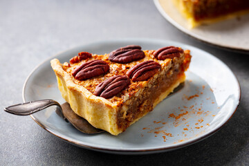 Pecan pie, tart slice on a white plate. Grey background. Close up.