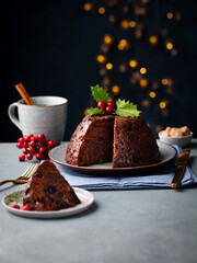 Christmas pudding, fruit cake with mug of tea. Traditional festive dessert. Dark background with lights garland. Copy space.