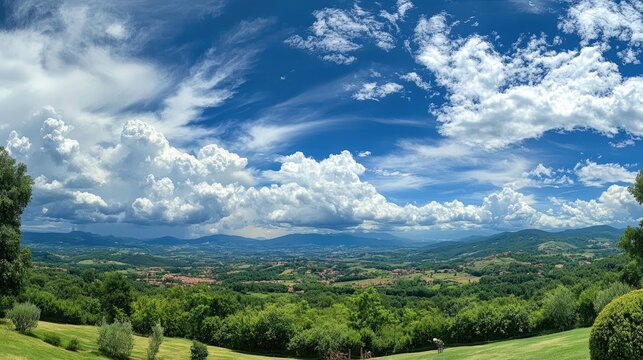 Panoramic summer landscape showcasing a vibrant blue sky adorned with fluffy white clouds over rolling green hills and valleys.