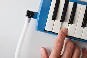 Detail of hand playing a melodica on a white table
