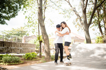 An incredibly cheerful couple is happily skating together in a beautiful sunlit park setting