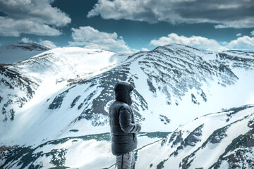 Serene man wearing a warm down jacket and hoodie, gazing at scenic view of snow-covered mountains...