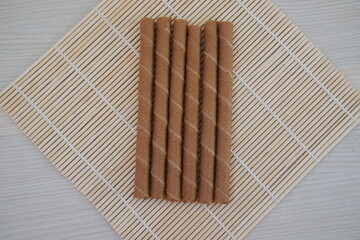 Six chocolate wafer rolls are neatly arranged in a row on a bamboo mat