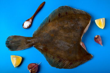 Fresh whole flounder without head on blue background. Around lemons, garlic and salt. Top view