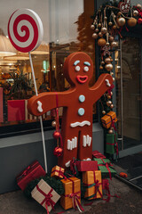 Cute outdoor Christmas decor of funny cartoon gingerbread man with lollipop and gifts at the entrance to the cafe