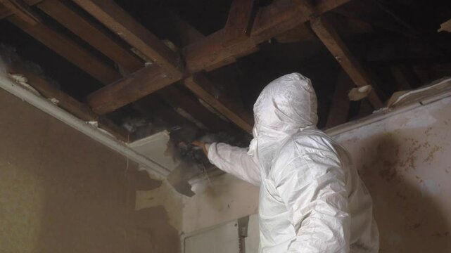 man in white overalls and a hammer removing the roof of a house