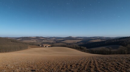 Fototapeta premium A vast, rolling landscape of fields and hills under a starry night sky.
