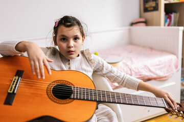 Little girl with autism plays guitar. Music therapy at home.