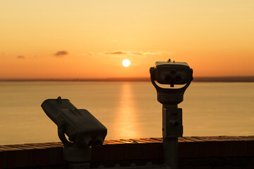 Binoculars on the terrace of Tihany Abbey. An amazing sunrise in the background, with the sun painting a golden line across Lake Balaton.