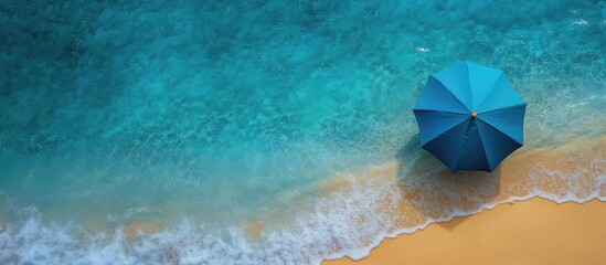 Aerial view of a vibrant blue beach umbrella on sandy shore with gentle waves, capturing a serene coastal escape for summer relaxation.