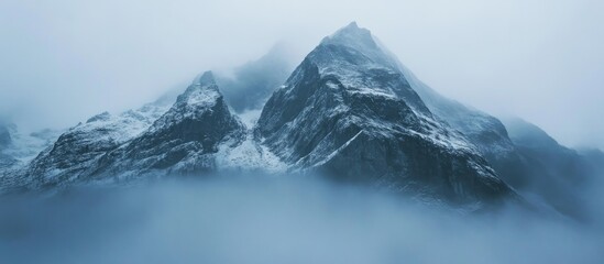 Obraz premium Majestic snow-capped mountain peaks shrouded in mist creating an atmospheric and serene landscape view in a rugged environment.