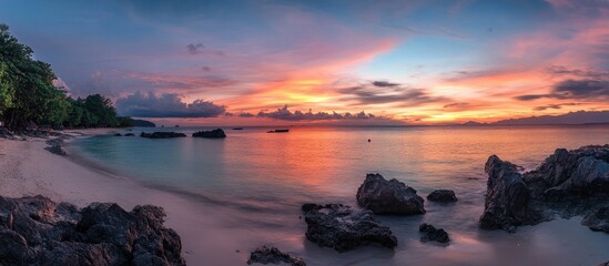 Vibrant sunset panorama illuminating tranquil beach and serene sea with rocky formations and lush greenery in the foreground