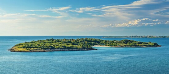 Obraz premium Serene coastal landscape of a lush green island under a clear blue sky on a sunny day with calm ocean waters surrounding it