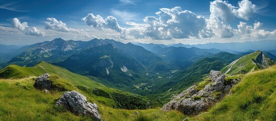 Fototapeta premium Majestic panoramic view of lush green mountains under a blue sky with fluffy clouds showcasing nature's beauty and tranquility.