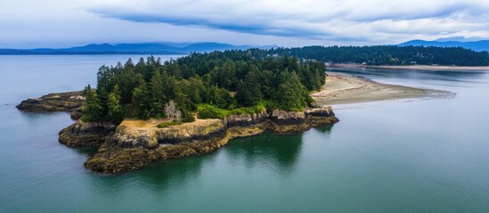 Obraz premium Drone view of a tranquil island coastline surrounded by calm waters and lush greenery under a cloudy sky