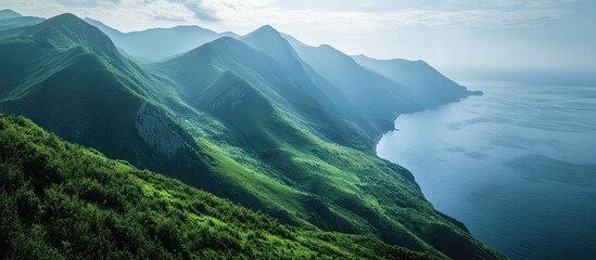 Fototapeta premium Lush green mountains cascading towards a tranquil sea under a serene sky showcasing natural beauty and peaceful landscapes