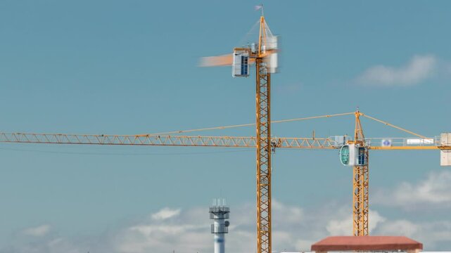 Timelapse of construction site with cranes working on a building complex. Dynamic clouds passing by in close-up view. Industrial progress under changing sky