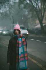 A woman in a pink hat and scarf stands on a foggy street