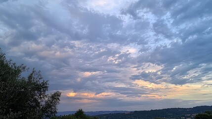 Scenic sunset view with colorful clouds over rolling hills and trees.