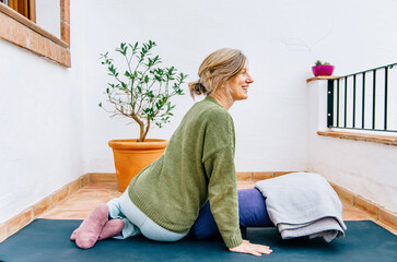 Woman in a warm outfit practising restorative yoga on a cosy outdoor terrace