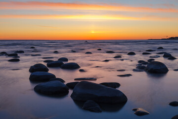 Sunset on the coast of the Baltic Sea. Stones on the shallow sea shore.