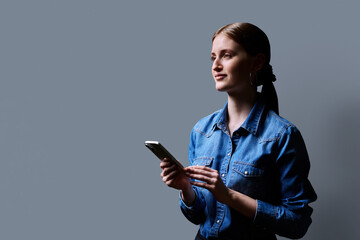 College student girl using smartphone, profile view, gray background