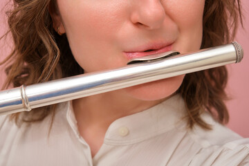 Close-up of woman playing a silver flute. Studio portrait on a pink background. Music and performance concept. © Андрей Журавлев