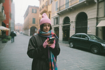 Fototapeta premium A woman stands on a busy street, focused on her cell phone