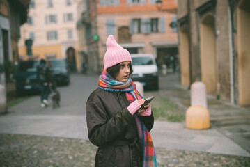 A woman in a pink hat and scarf is looking at her phone