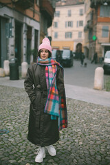 A woman in a pink hat and scarf stands on a cobblestone street