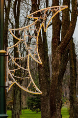Outdoor New Year decoration in the form of a fir tree with garlands against the background of a winter park with trees and green lawns, close-up.