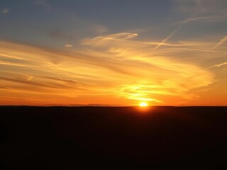 Vibrant oranges and yellows light up the summer sky as a breathtaking sunset unfolds against wispy clouds and long shadows stretching across the landscape, scenic view, outdoor scene, sunset