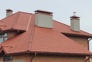 red tile roof of large private brown brick house with grey chimneys against sky on evening street