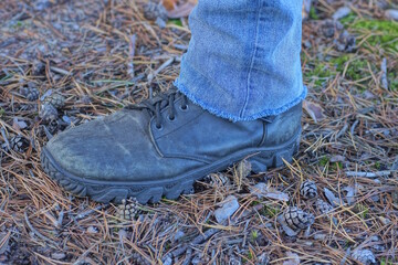 one black high leather boot on a foot stands on a  gray ground in summer nature