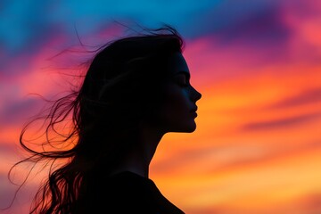 Silhouette of a serene woman with flowing hair against vibrant sunset sky, capturing moment of peace