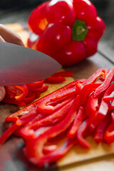 cook cutting red bell pepper on a board.