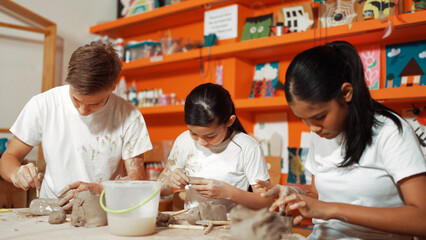 Happy diverse highschool student modeling clay at pottery workshop. Cute children with mixed raced working and making cup of clay by using carving equipment at art lesson. Creative class. Edification.